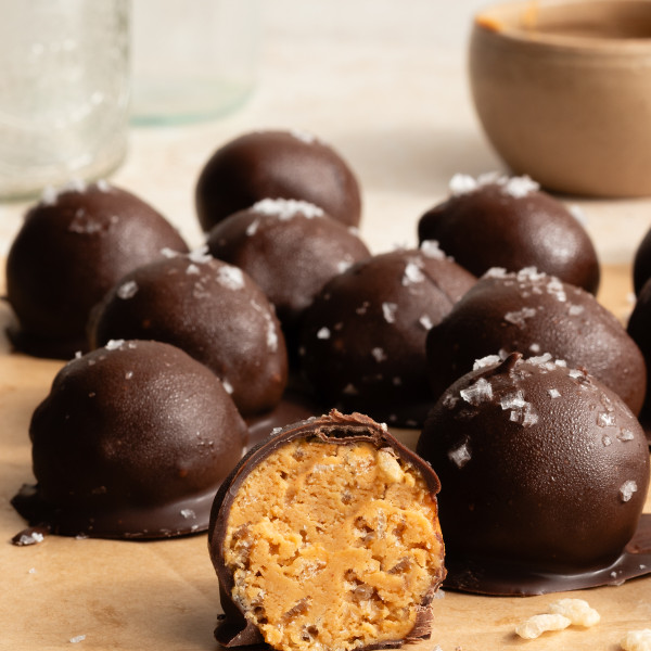 Crunchy peanut butter snack bite cut in half with more bites covered in chocolate behind it.