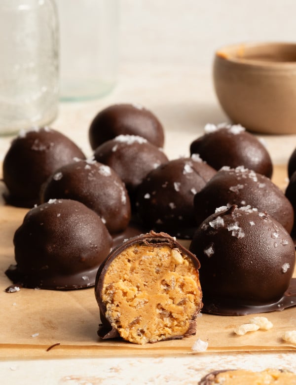 Crunchy peanut butter snack bite cut in half with more bites covered in chocolate behind it.