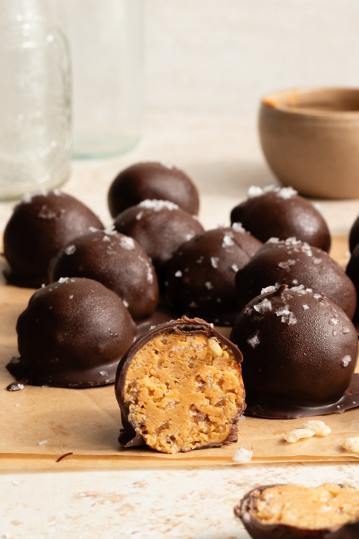 Crunchy peanut butter snack bite cut in half with more bites covered in chocolate behind it.