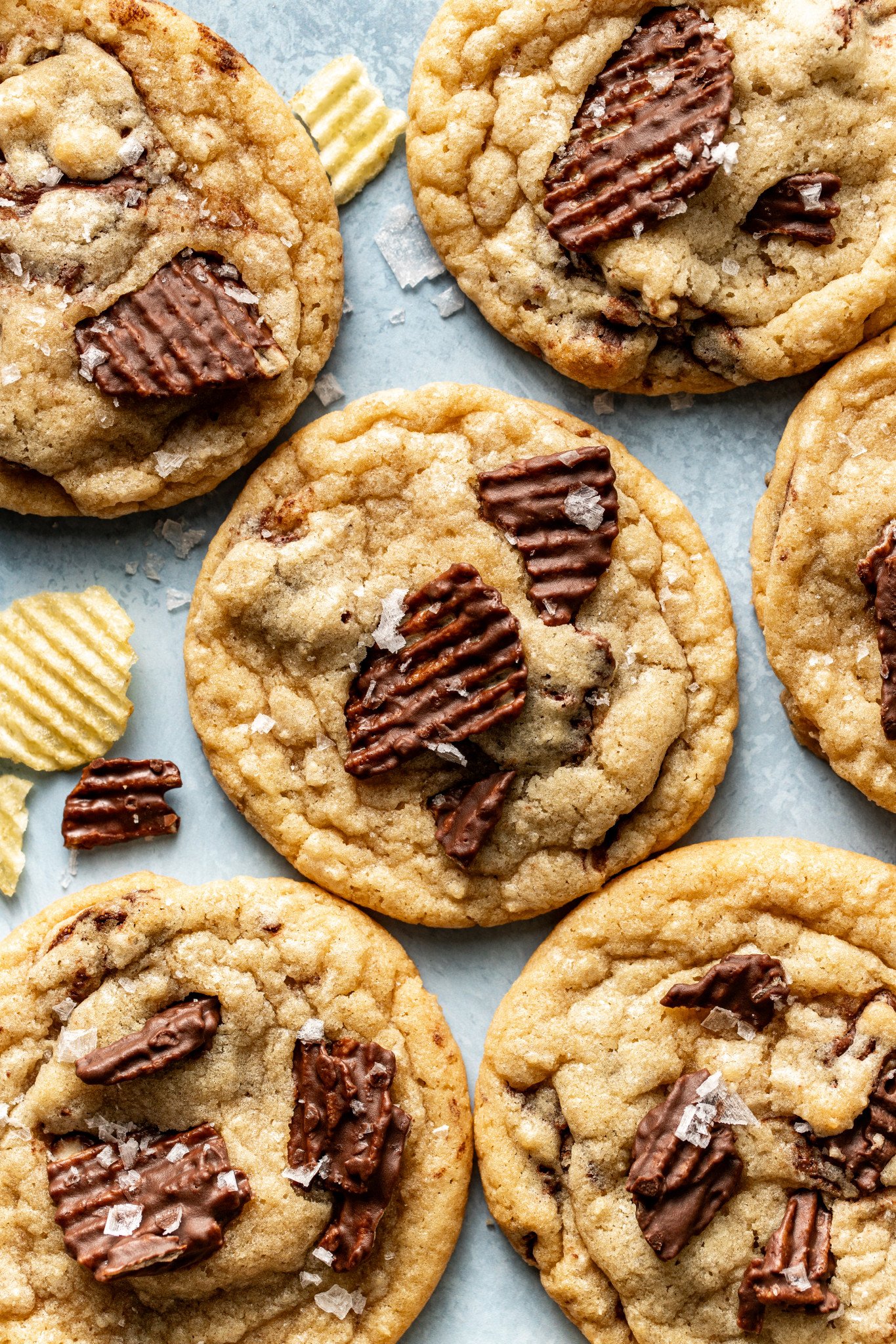 Baked chocolate potato chip cookies on table garnished with flaky sea salt.