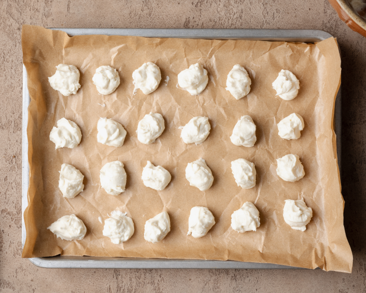 Balls of cheesecake filling on parchment-lined baking sheet before freezing.