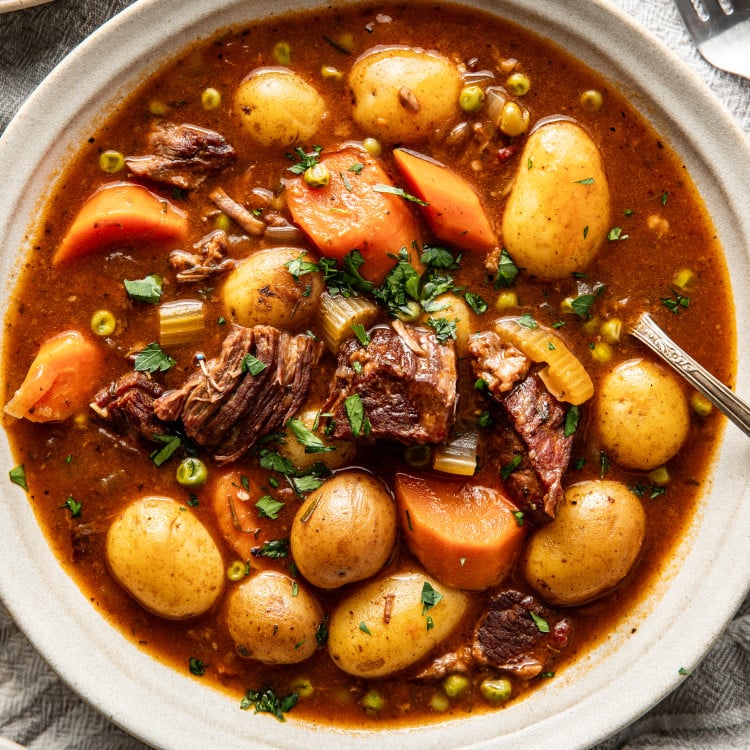 Slow cooker beef stew in white bowl with spoon, garnished with fresh parsley.