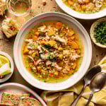 Two bowls of Lemon Chicken soup in bowls with bread, spoons, and parsley surrounding them.