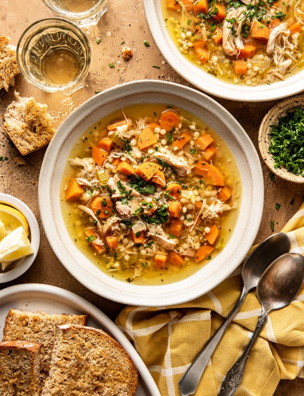 Two bowls of Lemon Chicken soup in bowls with bread, spoons, and parsley surrounding them.