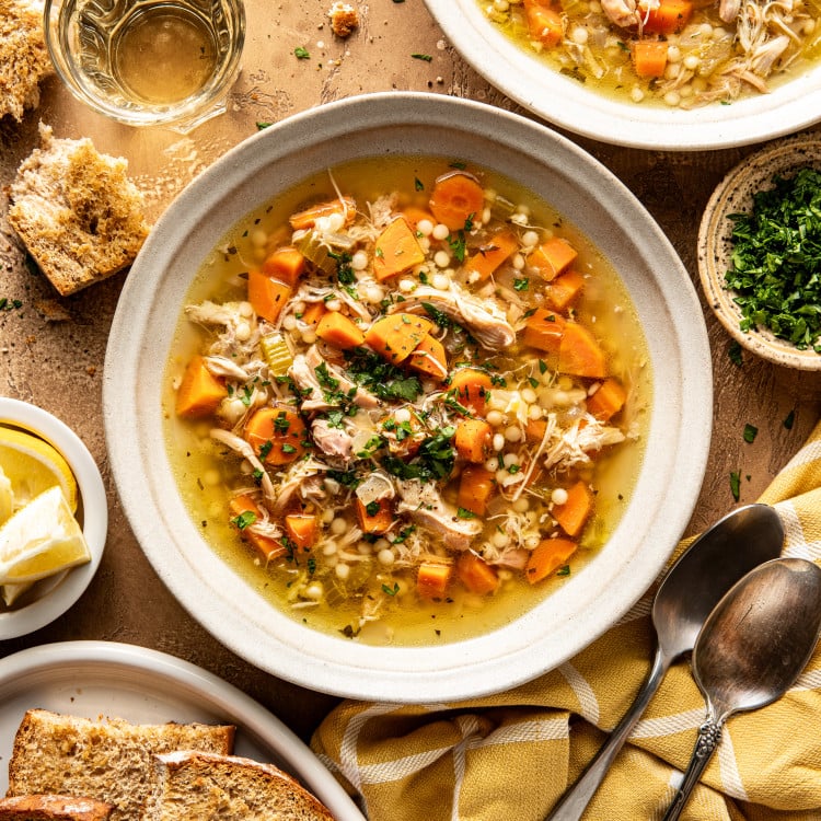 Two bowls of Lemon Chicken soup in bowls with bread, spoons, and parsley surrounding them.