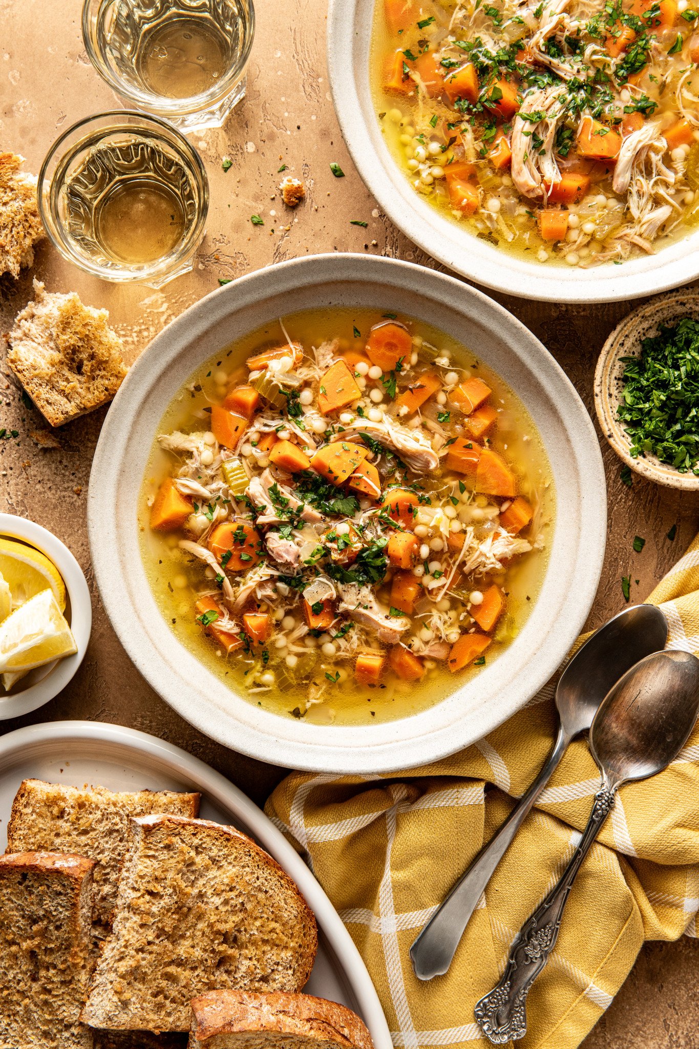 Two bowls of Lemon Chicken soup in bowls with bread, spoons, and parsley surrounding them.