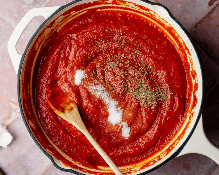 Adding the seasonings to tomato sauce in large skillet and mixing together with wood spoon.