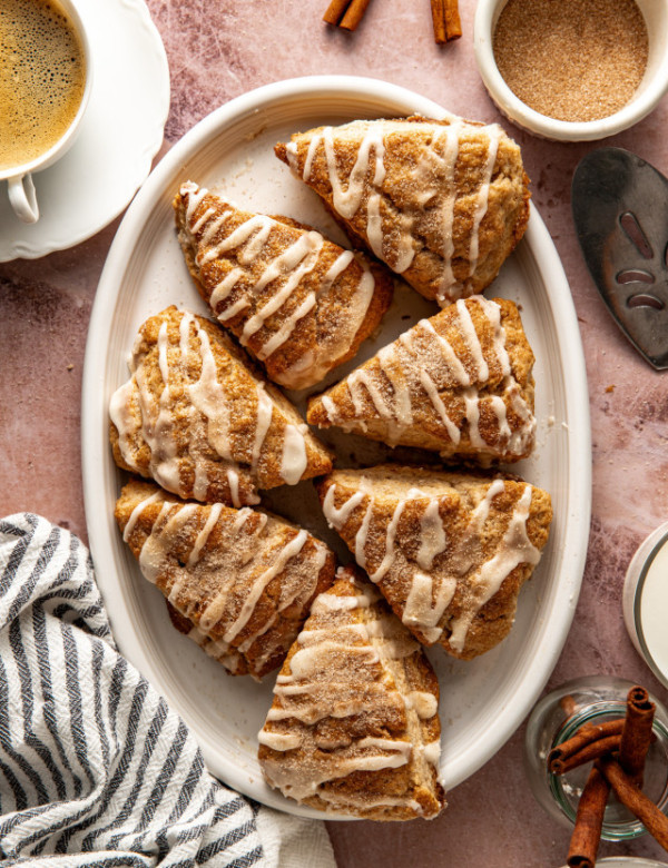 Seven cinnamon scones on white serving platter with cup of coffee off to the side.