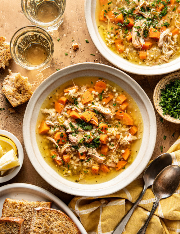 Two bowls of Lemon Chicken soup in bowls with bread, spoons, and parsley surrounding them.