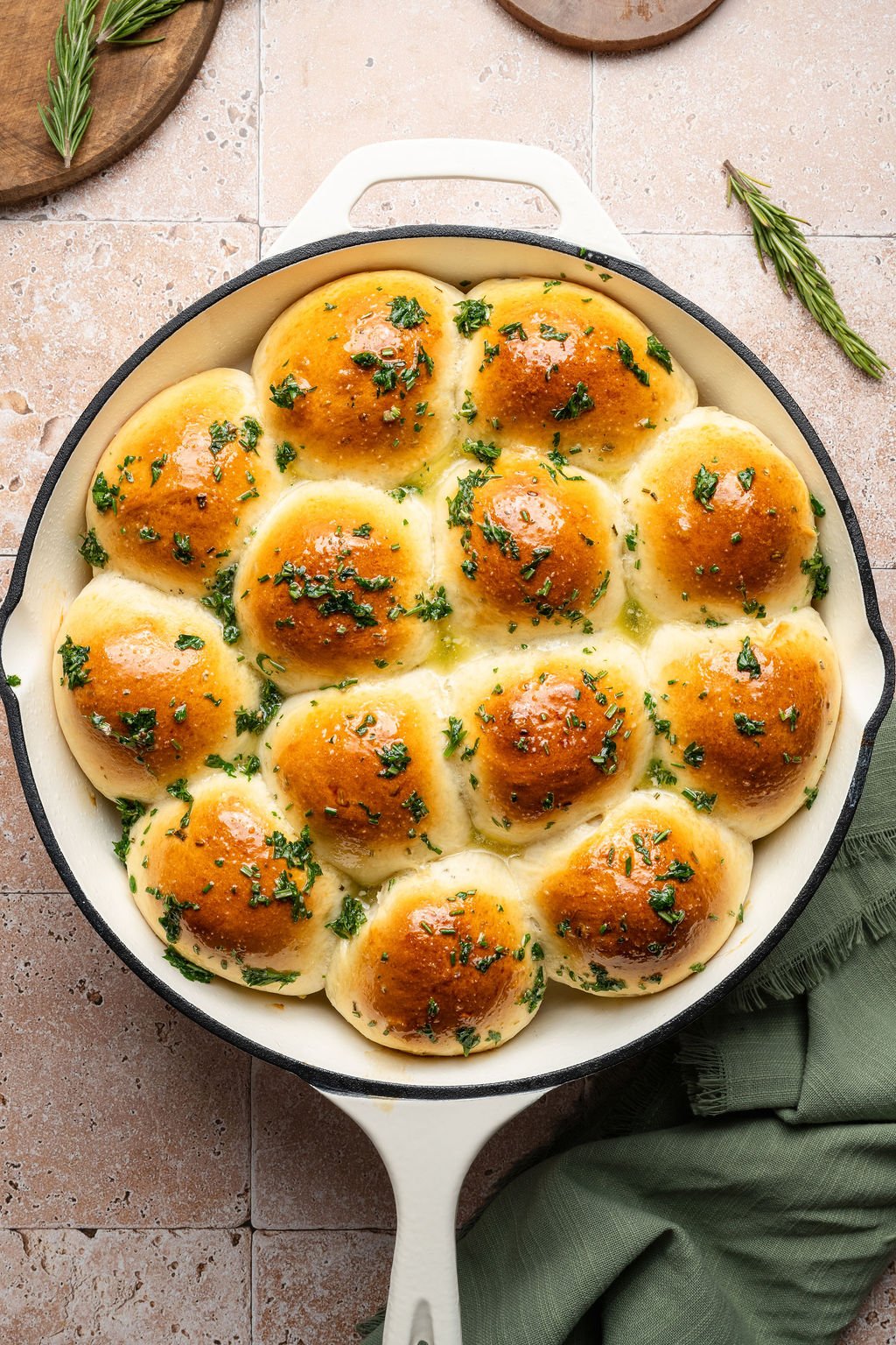 Overhead view of golden brown garlic rosemary pull-apart rolls in a white cast iron skillet, brushed with butter and sprinkled with fresh parsley.