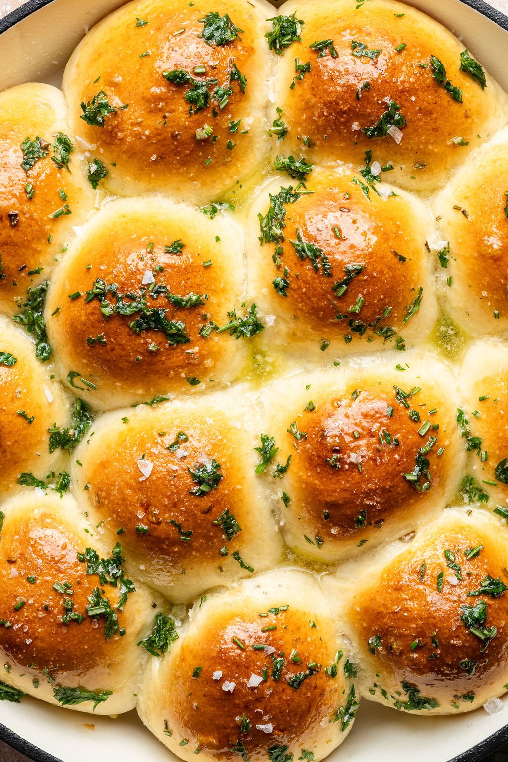 Close-up shot of fluffy garlic rosemary pull-apart rolls with shiny golden tops, melted butter, and fresh chopped herbs.