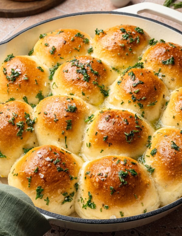 Overhead view of garlic rosemary rolls in a white skillet, baked until golden brown and finished with flaky sea salt and herbs.