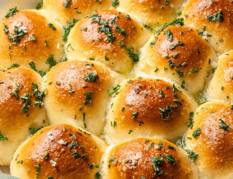 Overhead view of garlic rosemary rolls in a white skillet, baked until golden brown and finished with flaky sea salt and herbs.