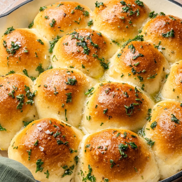 Overhead view of garlic rosemary rolls in a white skillet, baked until golden brown and finished with flaky sea salt and herbs.
