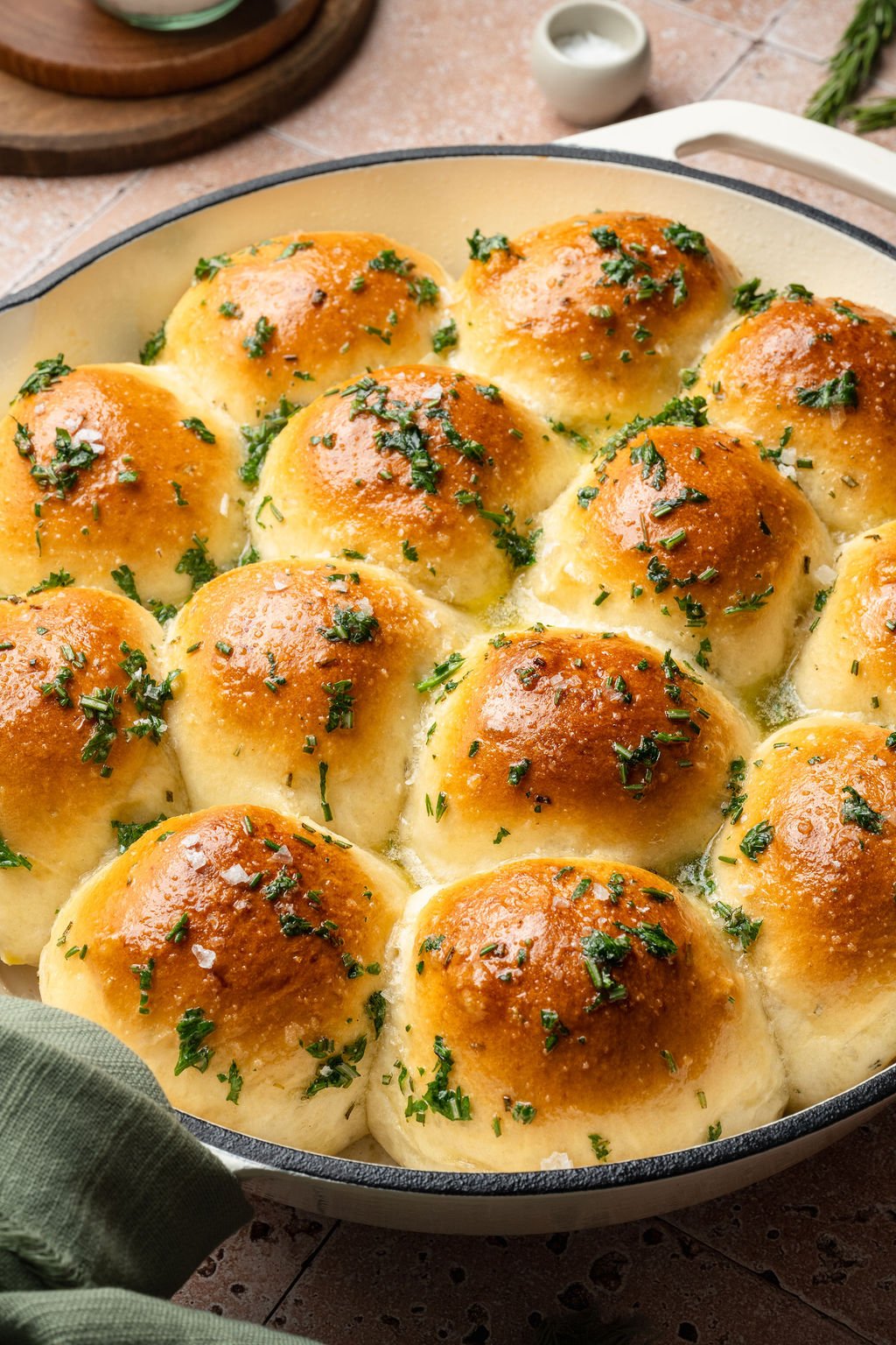 Overhead view of garlic rosemary rolls in a white skillet, baked until golden brown and finished with flaky sea salt and herbs.