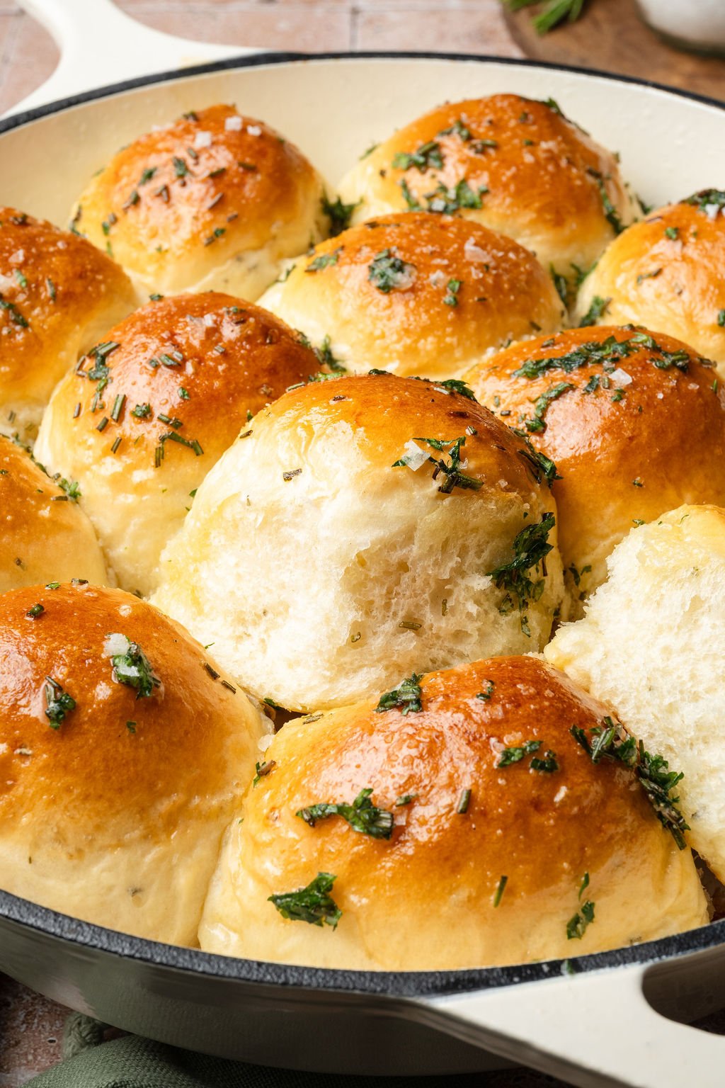 Garlic rosemary dinner rolls with one roll pulled out, showing the soft fluffy texture inside.
