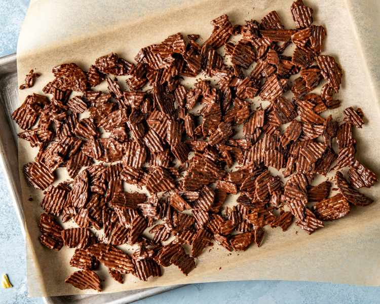 Pouring chocolate potato chips on parchment lined tray to let chocolate harden before adding to cookies.
