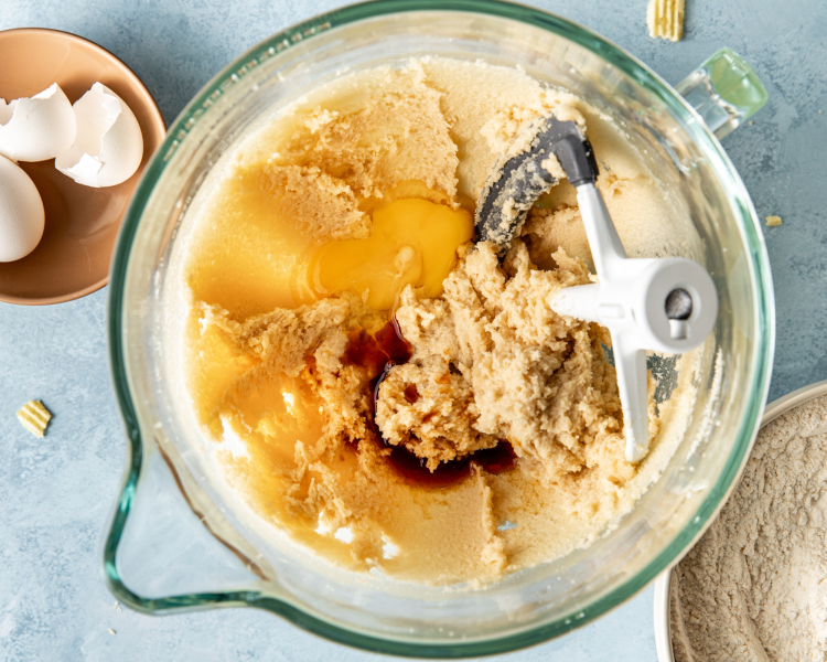 Adding eggs and vanilla to the beaten butter and sugars in glass mixing bowl.