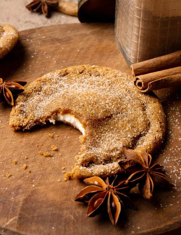 Pumpkin cheesecake cookie with bite taken out of the center on wood cutting board.