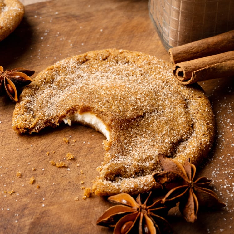 Pumpkin cheesecake cookie with bite taken out of the center on wood cutting board.