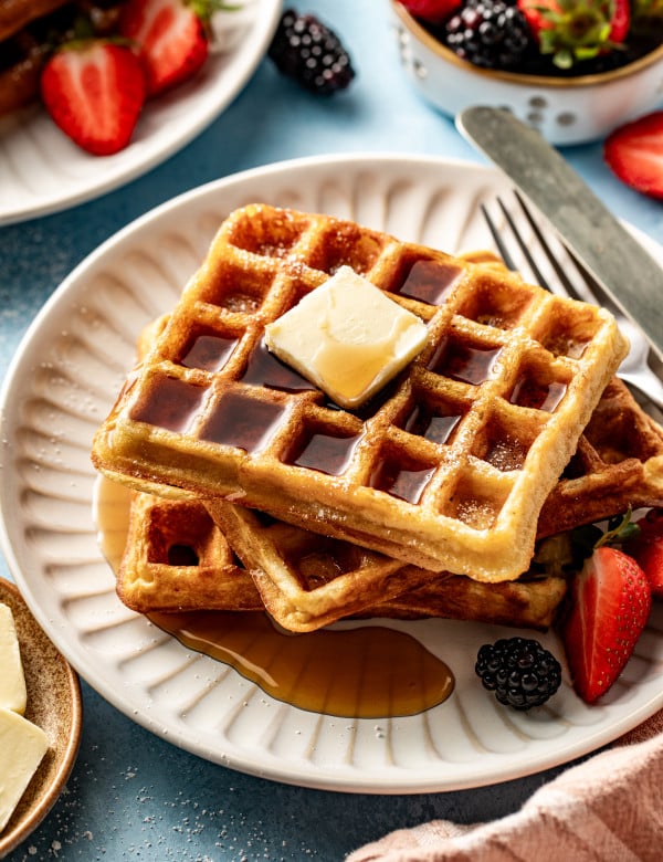 Buttermilk waffles stacked on plate topping with butter and syrup.