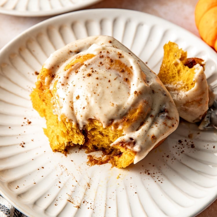 Pumpkin cinnamon roll broken in half on plate.