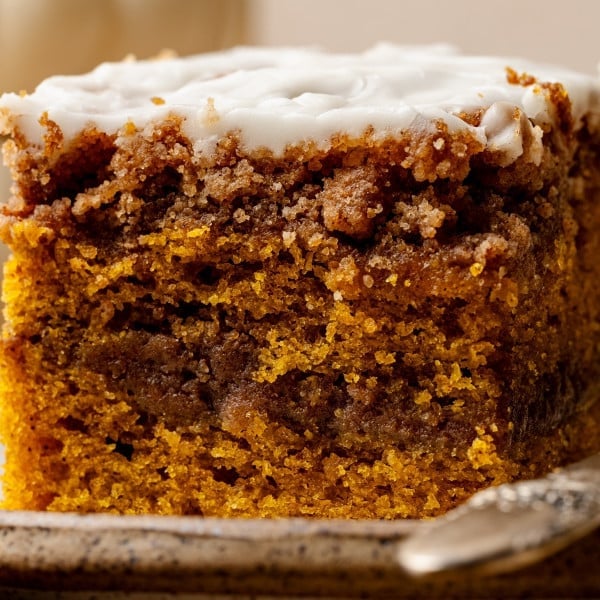 Close-up of a baked slice of pumpkin coffee cake with a cinnamon swirl and maple glaze on top, served on a plate with a fork.