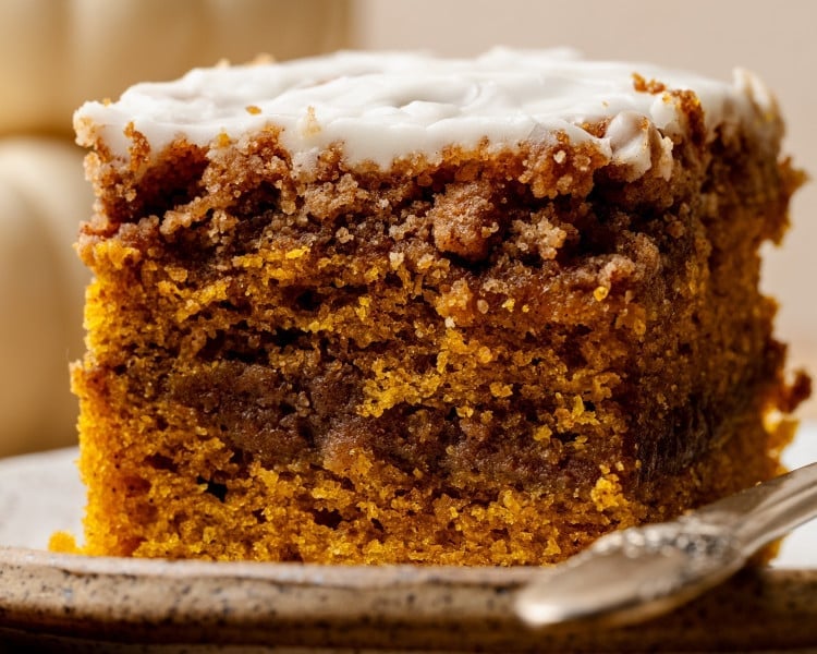 Close-up of a baked slice of pumpkin coffee cake with a cinnamon swirl and maple glaze on top, served on a plate with a fork.