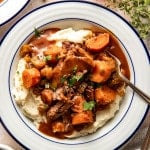 Slow cooker pot roast served over mashed potatoes in a white serving bowl with fork.