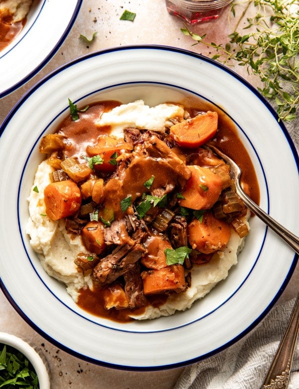 Slow cooker pot roast served over mashed potatoes in a white serving bowl with fork.