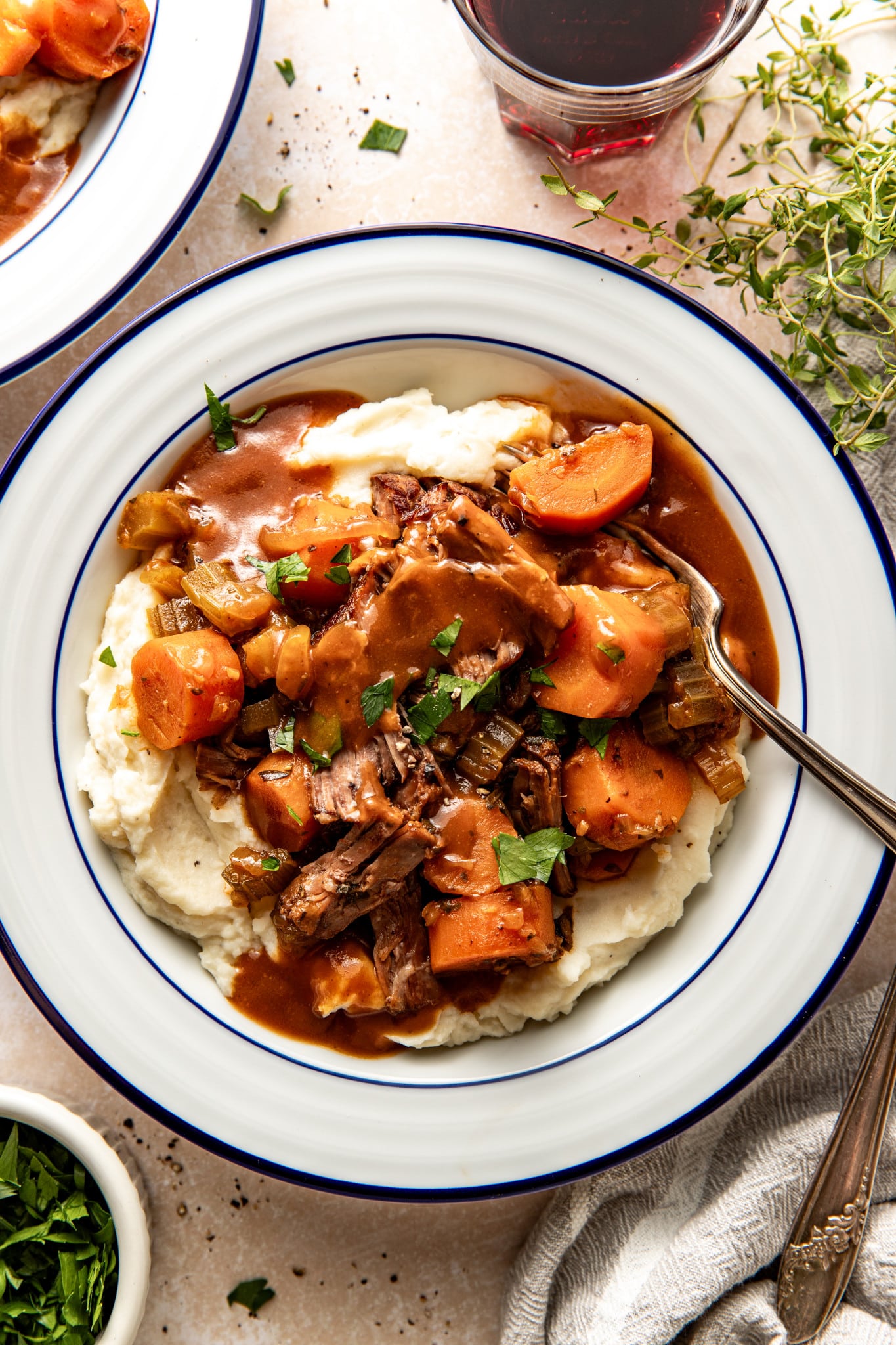 Slow cooker pot roast served over mashed potatoes in a white serving bowl with fork.