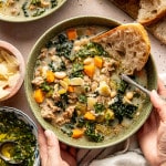 Sausage, kale and white bean soup in bowl with a side of crusty bread and spoon in bowl.