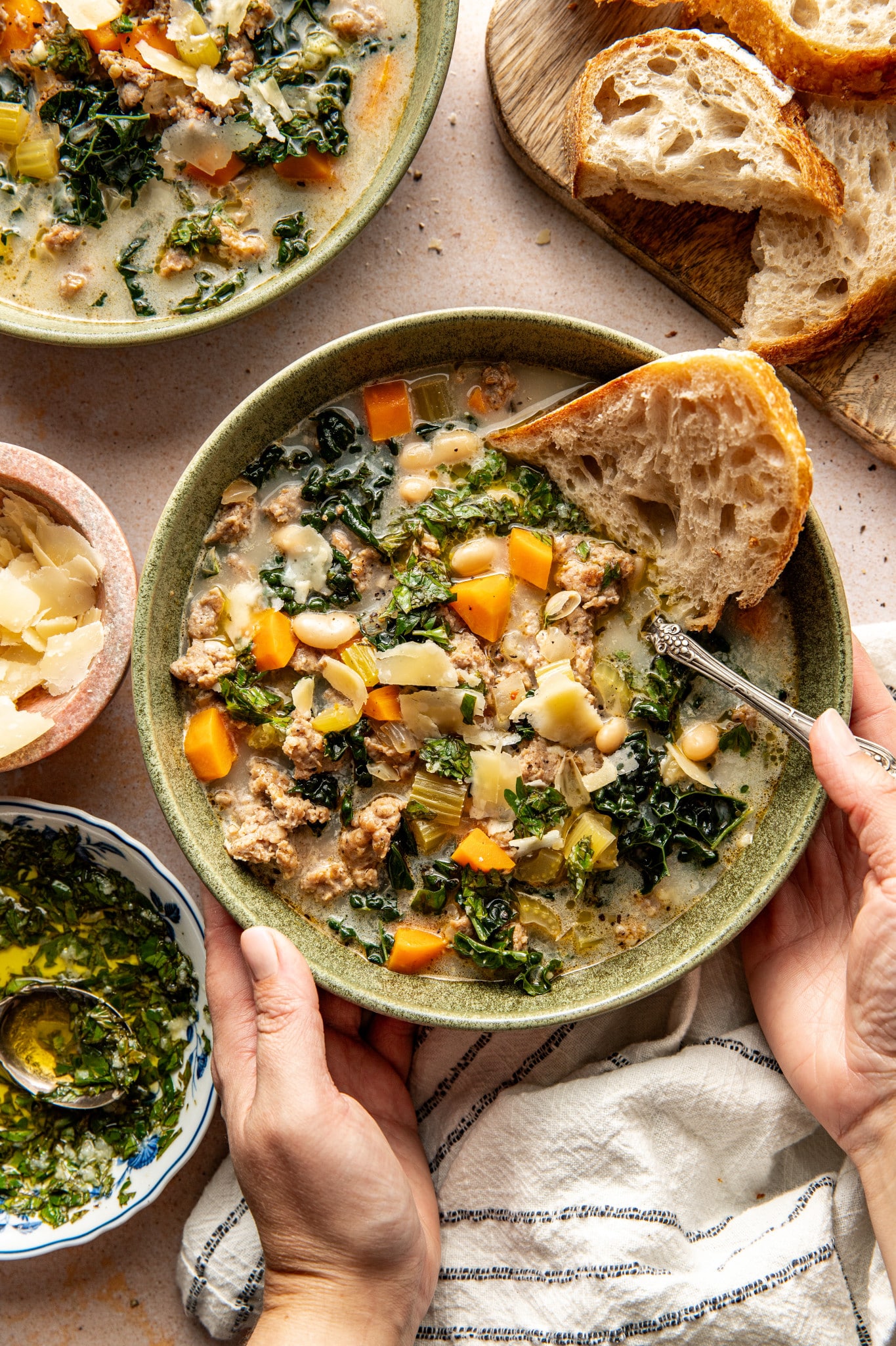 Sausage, kale and white bean soup in bowl with a side of crusty bread and spoon in bowl.