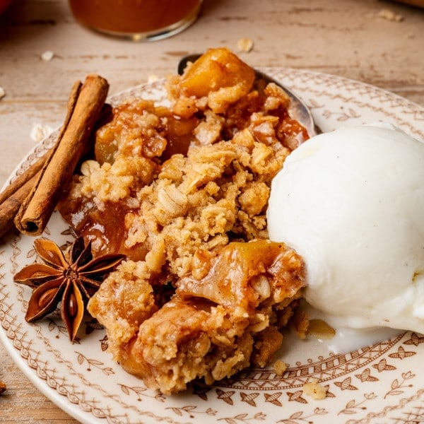 Apple crisp served on plate with scoop of vanilla ice cream and garnished with cinnamon sticks and cloves.