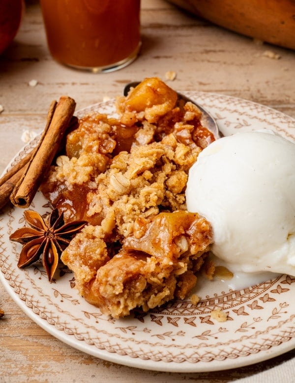 Apple crisp served on plate with scoop of vanilla ice cream and garnished with cinnamon sticks and cloves.