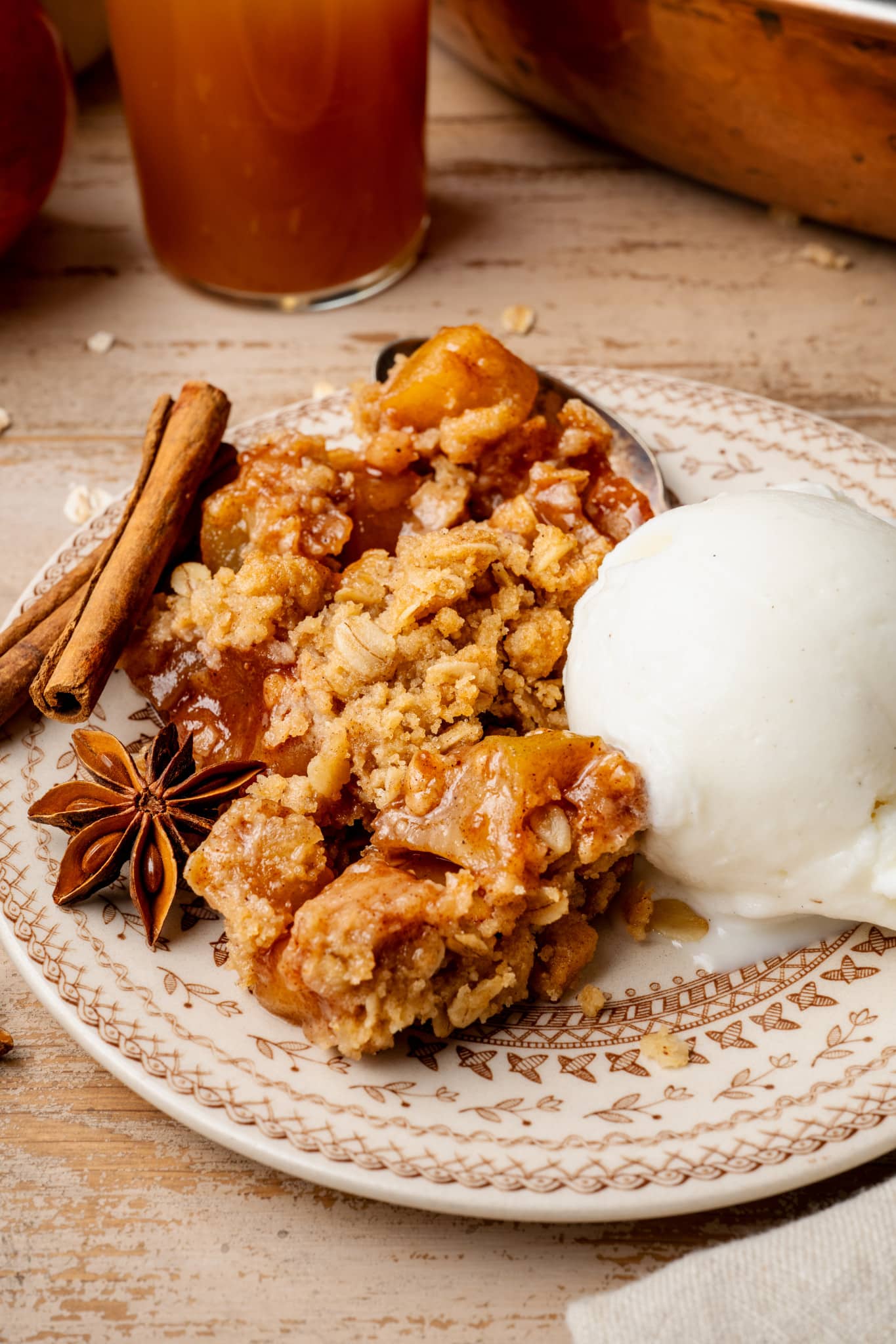 Apple crisp served on plate with scoop of vanilla ice cream and garnished with cinnamon sticks and cloves.