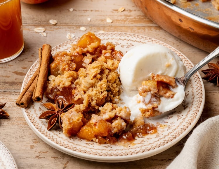Apple crisp and scoop of vanilla ice cream on plate with spoon.