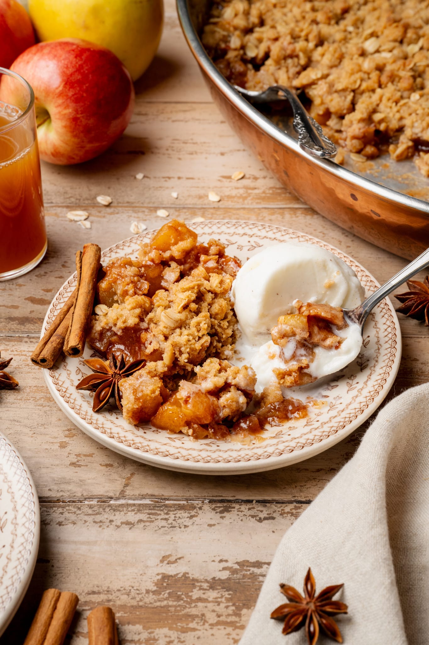 Apple crisp and scoop of vanilla ice cream on plate with spoon.