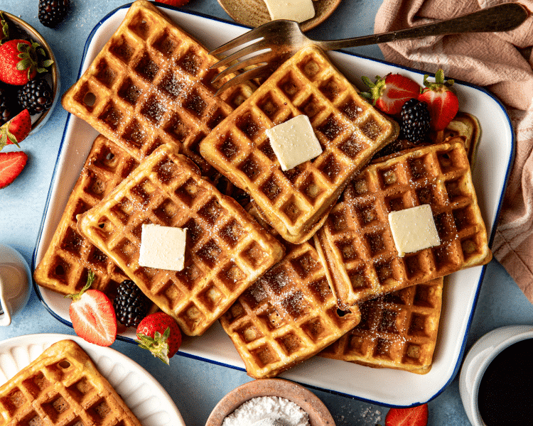 Plate of buttermilk waffles topped with butter and powdered sugar.