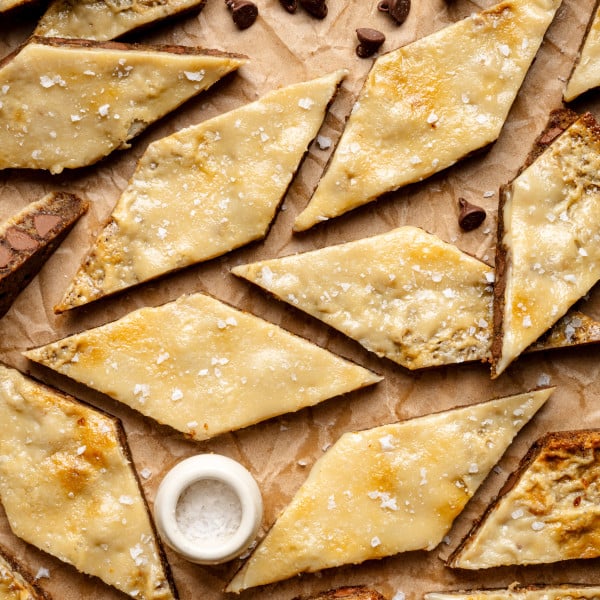 Coffee cookie bars cut into diamond-shapes on parchment paper with small bowl of flaky salt and chocolate chips.