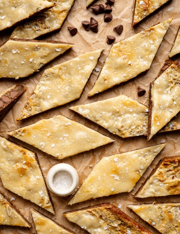 Coffee cookie bars cut into diamond-shapes on parchment paper with small bowl of flaky salt and chocolate chips.