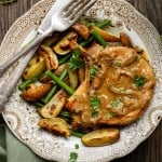 Slow cooker pork chop on plate with potatoes and green beans with knife and fork.