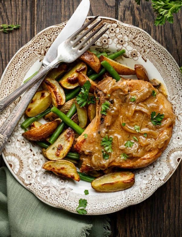 Slow cooker pork chop on plate with potatoes and green beans with knife and fork.
