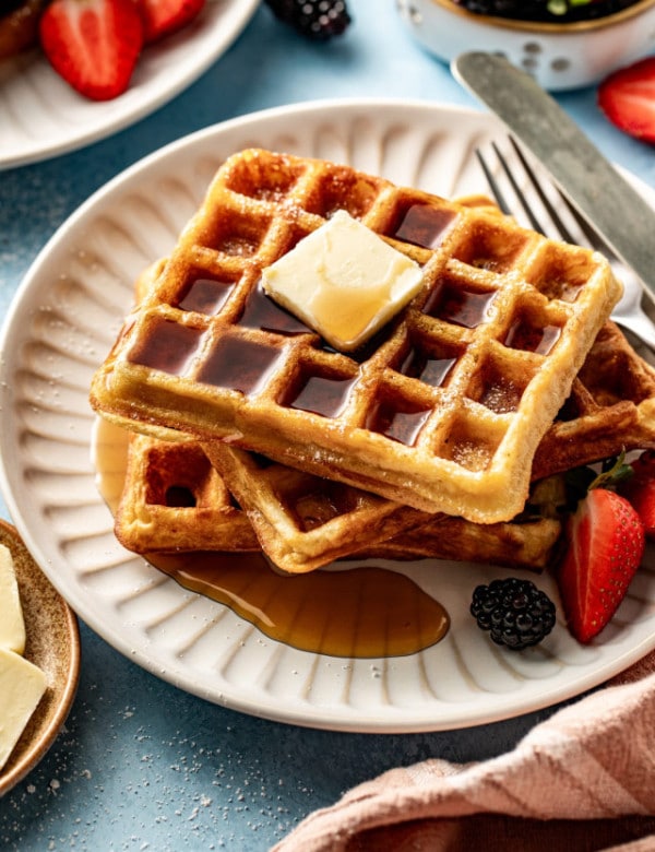 Buttermilk waffles stacked on plate topping with butter and syrup.