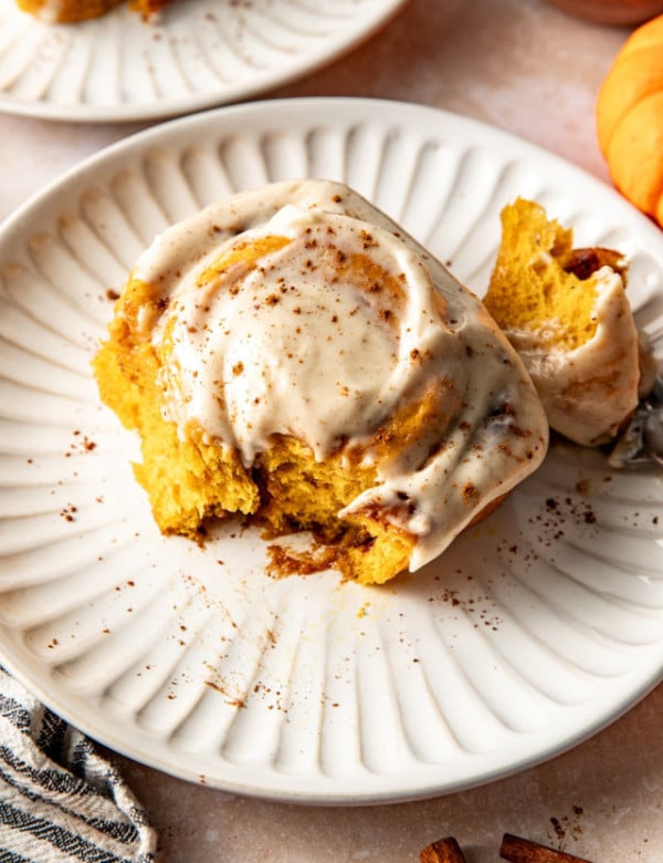 Pumpkin cinnamon roll broken in half on plate.