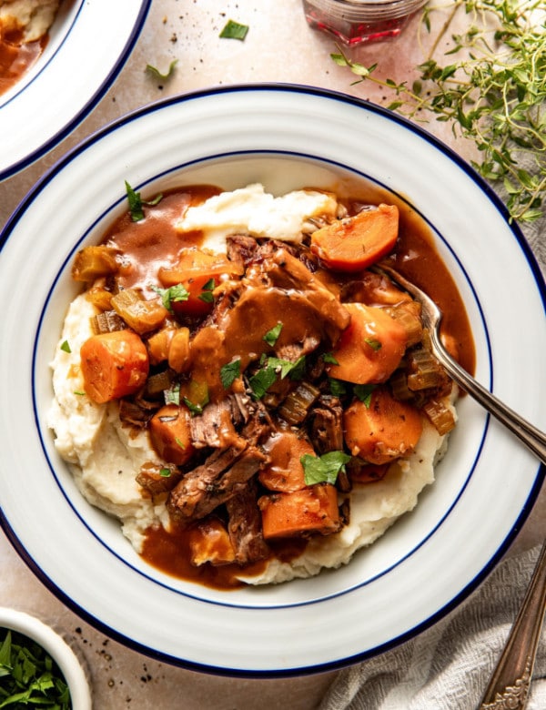 Slow cooker pot roast served over mashed potatoes in a white serving bowl with fork.