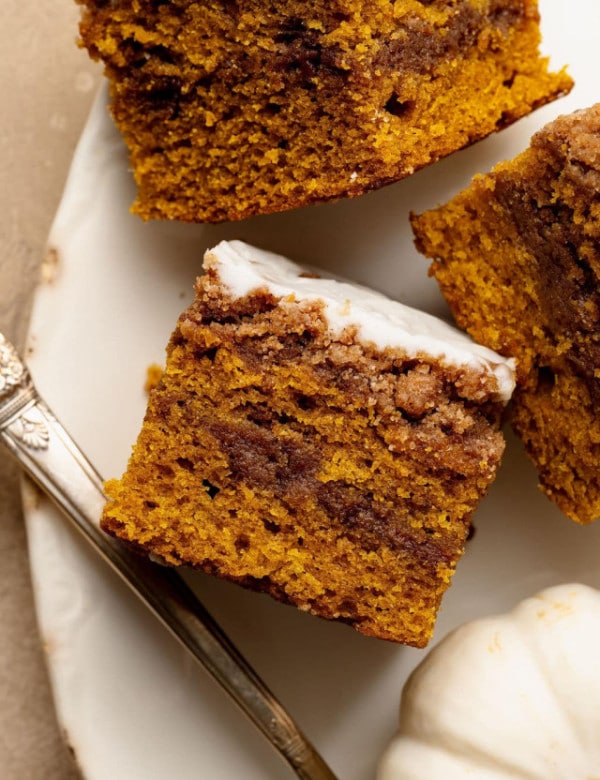 Overhead view of pumpkin coffee cake slices on a plate with a white pumpkin nearby, showing the glaze and swirl details.