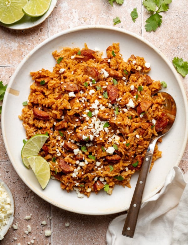 Spanish rice and chorizo on plate garnished with lime wedges and spoon on side of plate.