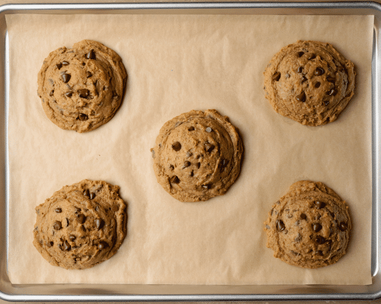 Six pumpkin chocolate chip cookies baked on a parchment-lined baking sheet.