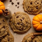 Pumpkin chocolate chip cookies topped with extra chocolate chips on parchment paper.